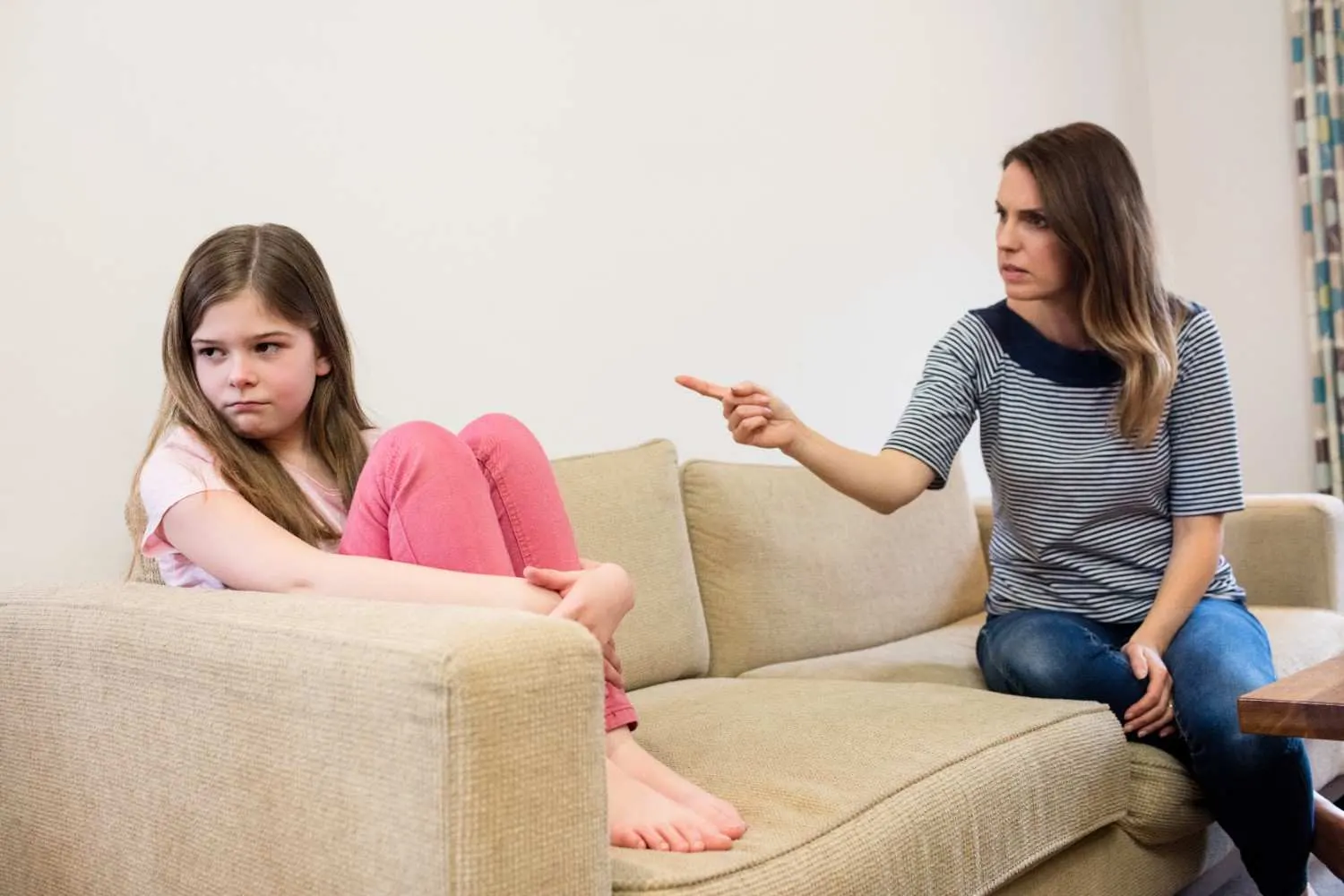 Mother pointing while child sits upset on sofa, showing tension during family conflict or dispute