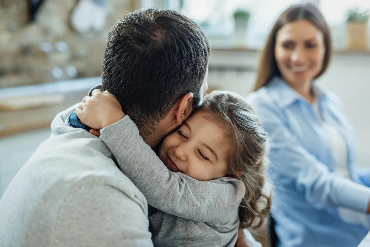 Young girl hugging her father while mother smiles in the background at home