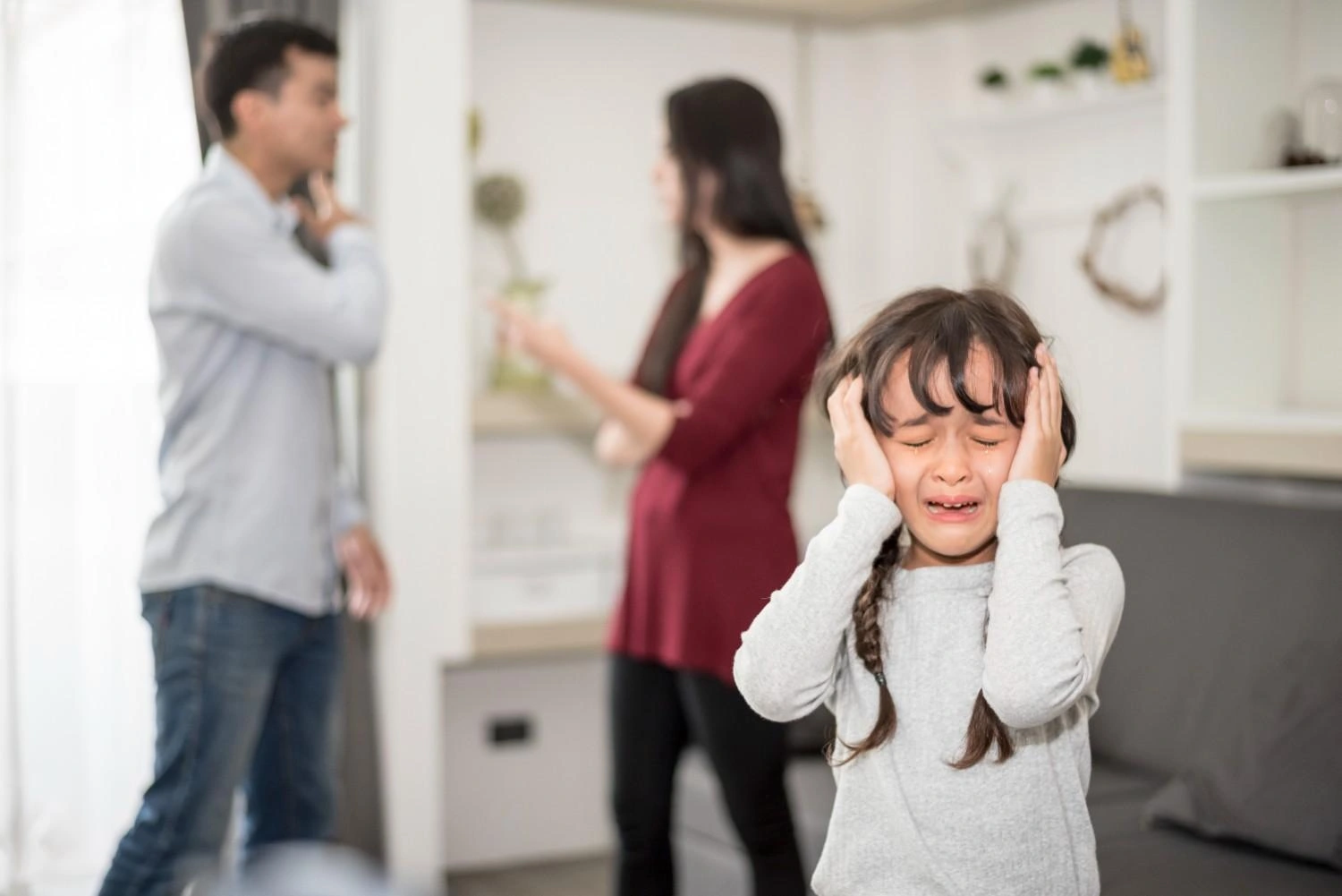 Child crying while parents argue in the background during a family conflict at home.