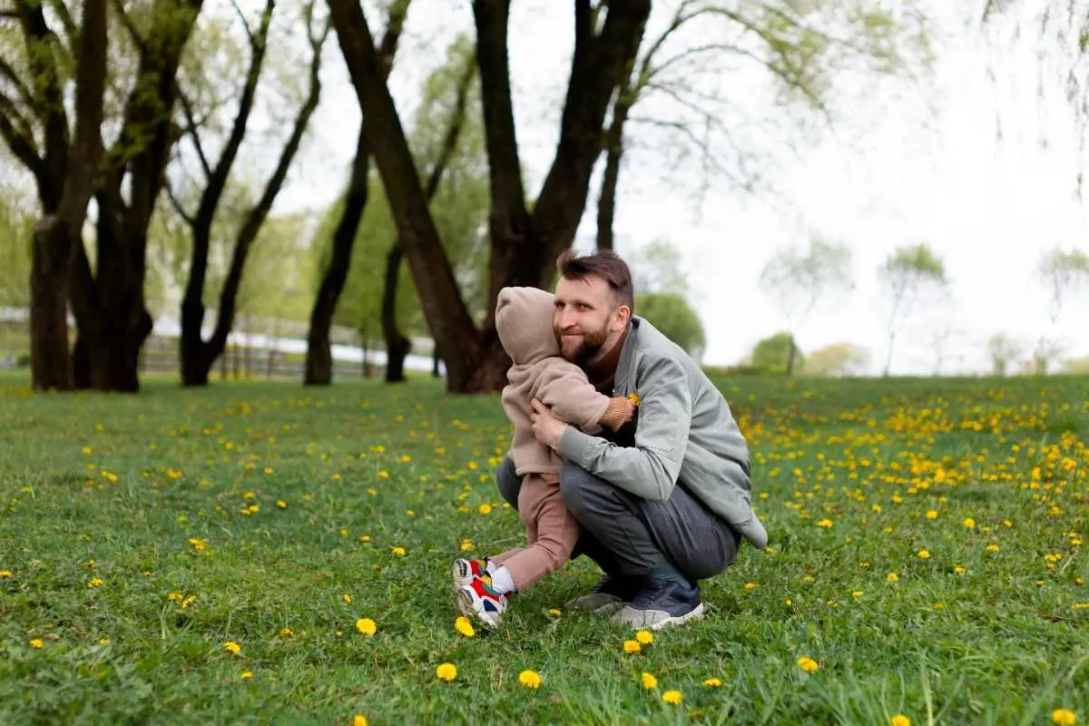Father hugging his young child outdoors in a green park.
